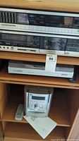 Photo showing JVC stereo cassette deck, JVC digital synthesizer stereo receiver in wooden shelving unit with Sony micro Hi-Fi system below and remote control on shelf.