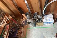 Hand tools, wooden organizer with hand tools, pipe wrenches, metal duct pieces, and flexible conduit in basement corner