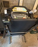 Front view of treadmill console and foldable deck, showing control buttons and cup holders with a rolled-up paper inside one cup holder.