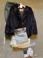 Overview photo of the vintage fur jacket, cream scarf, and gloves placed on carpet with jacket on hanger.