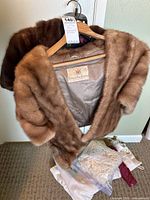 Overall view of both fur stoles draped on hanger with cloth pouches and zip bags at base