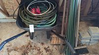 Wheelbarrow loaded with coiled garden hoses, garden stakes, and other garden items in shed with a dirt floor