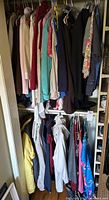 Closet rod with assorted women's clothing hanging including tops, jackets, cardigans, and dresses in various colors and fabrics.