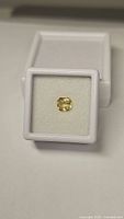 Yellow cushion cut sapphire gemstone in white display box, showing bright yellow color and clarity.