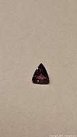 Natural pink-purple trillion cut sapphire gemstone laid on a plain background to show cut and color.