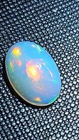 Close-up image of a natural Ethiopian opal cabochon on a textured black surface showing vivid rolling play of color.