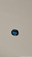Oval cut deep dark lagoon blue London Blue Topaz gemstone with brilliant facets visible on neutral background.