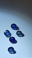 Five round cut royal blue sapphires arranged together showing variations in color and clarity under light.