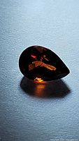 Close-up photo of a single pear cut spessartite garnet gemstone showing fire orange color and facet reflections.