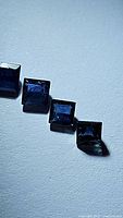 Four square princess cut deep blue sapphires arranged in a row on a light surface with some visible inclusions.
