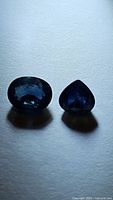 Pair of natural blue sapphires, one oval cut and one pear-shaped on a white background.