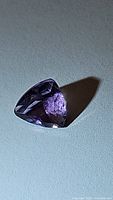 Close-up image of a purple trillion cut amethyst gemstone casting a shadow on a grey surface.