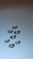 Seven pear cut aquamarine gemstones arranged on a white surface under natural light, showing size and clarity.