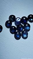 Close-up photo showing multiple round deep blue sapphire stones with visible reflections and consistent size.