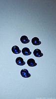 Eight natural round-cut royal blue Ceylon sapphires arranged on a flat surface, showing color and facets.
