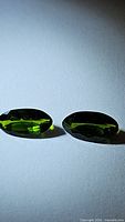 Two oval faceted green chrome diopside stones placed side by side showing size and color match.