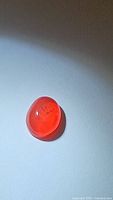 Natural bright fire orange Ethiopian fire opal, oval cabochon, placed on white surface, showing its translucent deep orange hue with internal features visible.