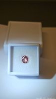 Natural pink Padparadscha colored oval cut untreated tourmaline gem securely placed in white jewelry box, showing color and clarity.