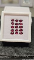 Fifteen oval cut deep pink purple Rhodolite garnet gemstones arranged in a white jewelry tray, total approximately 5.37ct
