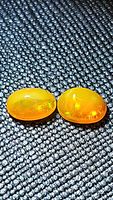 Close-up photo of two oval cabochon orange fire opals on black textured background showing play of color.
