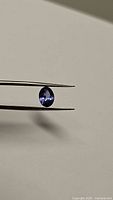 Close-up photo of oval cut tanzanite held with tweezers, showcasing deep violet-blue color and clarity.