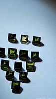 Multiple natural green tourmaline princess cut gemstones displayed on white background, showing color and clarity under light.