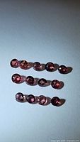 Photo showing 13 small round-cut sapphires in varying pink-red hues base-lit on white background in three rows.