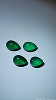 Five vivid green pear-shaped onyx cabochon gemstones lying on a white surface under lighting, showing glossy smooth surfaces and color uniformity.