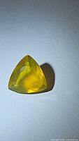 Natural yellow fire opal gemstone, trillion cut shape, showing clarity and color under light.