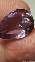 Close-up front view showing pear-shaped amethyst held against finger with visible rainbow inclusion near the surface.