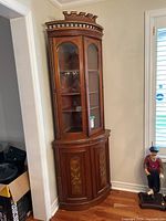 Full view of the antique corner china cabinet showing height, wood finish, crown molding, glass doors with shelves inside, and painted lower doors.