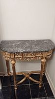 Front view of half-round gilt console table with veined marble top against white wall