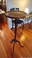 Full view of antique wooden plant stand showing round top and tripod base on hardwood floor.