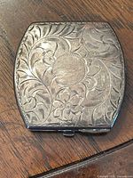 Top view of the closed silver compact showing engraved floral and leaf pattern.