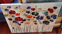 Front view of unframed canvas art painting showing vibrant flowers in multiple colors including red, purple, yellow, orange, blue, and green on a light background.