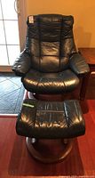 Front view of black leather recliner chair and matching ottoman on wood bases