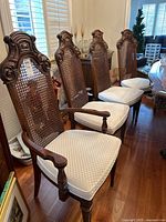 Four of the dining chairs shown in a row, featuring dark wood frames, cane backs, and white upholstered seat cushions