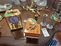 Kundo brass and glass carriage clock, wooden piano music box, metal salt shaker music box, pewter and metal candleholders on a wooden table
