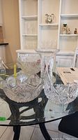 Photo showing two crystal bowls and one vase on a glass table, clear intricate cut glass patterns visible.