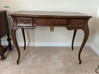 Front view of desk showing curved legs, three drawers, faux leather top