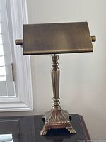 Front view of brass desk lamp showing triangular shade and detailed fluted column base.