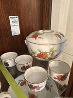 Single view of covered casserole dish with fruit design and gold trim, along with four ramekins each decorated with different fruit motifs.