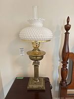 Full view of the lamp showing metal base, milk glass hobnail shade with ruffled edge, and clear glass chimney.
