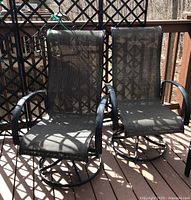 Two matching outdoor patio swivel chairs on wood deck, black metal frames with mesh fabric seats and backs, showing some scuffs on frames.