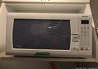 Front view of Panasonic microwave showing the door and control panel with buttons and display.