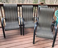 Four matching outdoor patio chairs on deck, showing mesh seats and backs with black metal frame, some wear visible.