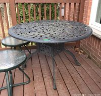 Full view of round cast iron patio table with ornate scrollwork and four curved legs on wooden deck.