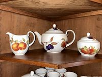 Teapot, creamer, and sugar bowl displayed on a wooden shelf, showing overall set design and decoration.
