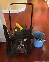 Front angled view showing Stanley vacuum with hoses and attached nozzle with blue bucket beside it.