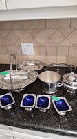 Full set displayed on countertop including the tureen, casserole holder, wine bottle holder, basket style dishes, and four small dishes with blue glass inserts.